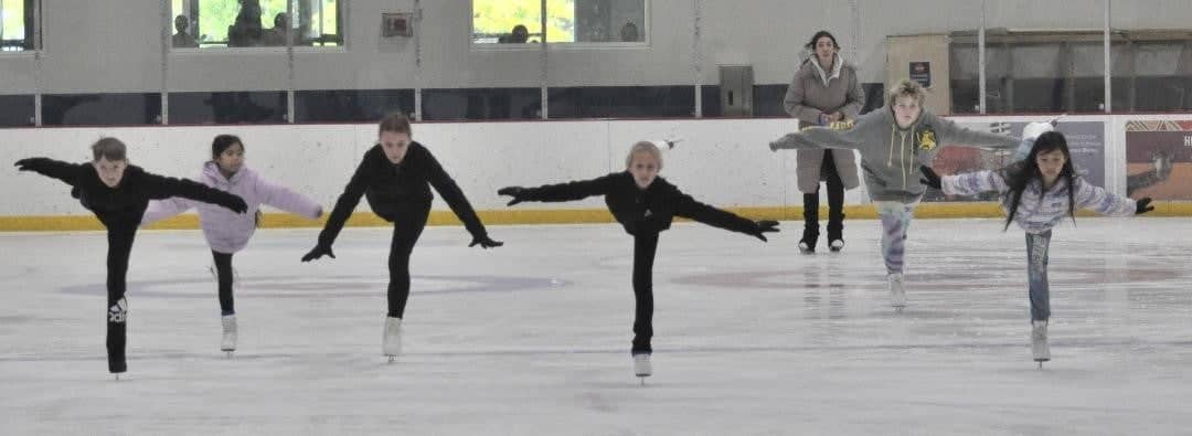 Coach Bianca Chal, wearing a tan coat, watches from behind, her students glide on the ice.